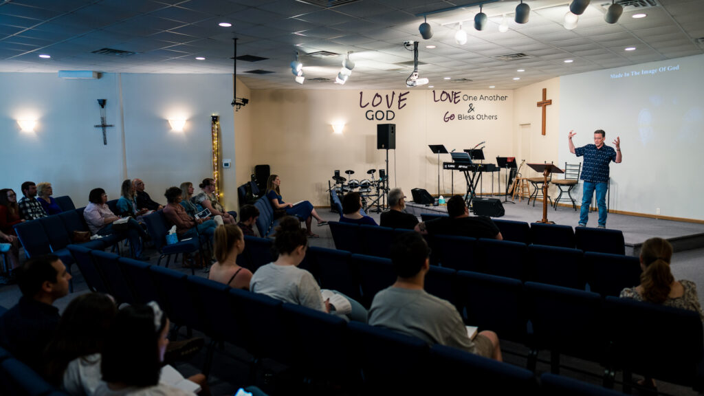 sanctuary on a sunday. people sitting in pews. Pastor talking with his arms up in the air.